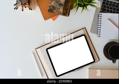 Vue de dessus de l'espace de travail avec tablette numérique à écran vierge, livre d'époque, ordinateur portable, maison et fournitures de bureau. Banque D'Images