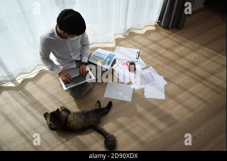 Homme avec son chat travaillant de la maison sur parquet dans la salle de séjour. Banque D'Images