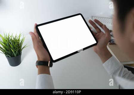 Prise de vue rognée d'un jeune designer professionnel tenant une tablette à écran vierge dans un espace de travail minimal. Banque D'Images