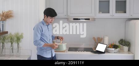 Jeune homme utilisant la tablette numérique et la cuisine moderne dans la cuisine. Banque D'Images