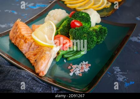 servir le saumon avec du citron, du brocoli et des légumes. Deux morceaux de saumon grillé sont servis sur une belle assiette Banque D'Images