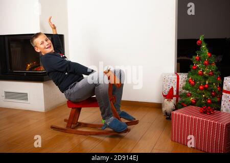 Un garçon à cheval en bois près de l'arbre de Noël Banque D'Images