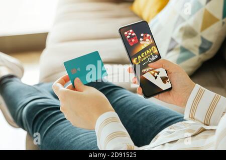 Photo d'une femme méconnaissable qui va jouer au casino en ligne depuis le canapé et qui tient une carte de crédit pour payer. Jeu en ligne et concept de pari Banque D'Images