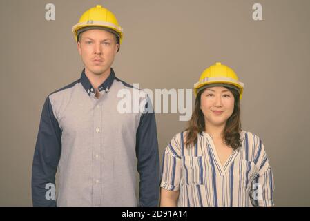 Jeune homme d'affaires élégant et femme d'affaires asiatique mature portant un casque sur fond gris Banque D'Images