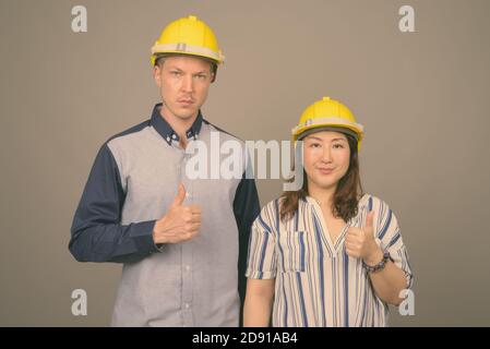 Jeune homme d'affaires élégant et femme d'affaires asiatique mature portant un casque sur fond gris Banque D'Images