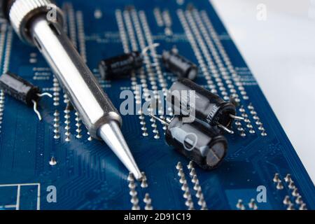 Fer à souder sur l'arrière-plan d'une carte d'ordinateur et condensateurs en mise au point. Le concept de réparation et de service Banque D'Images
