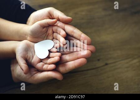 Cœur en papier blanc dans les paumes des enfants et des femmes, vue du dessus. Amour, fête des mères, concept de famille. Banque D'Images