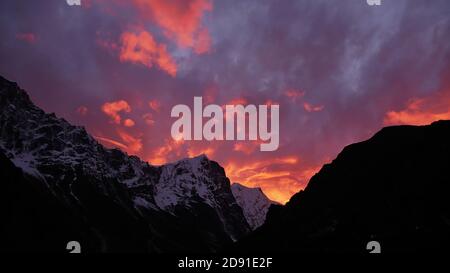 Coucher de soleil impressionnant sur une chaîne de montagnes enneigée dans l'Himalaya près de Thame, parc national de Sagarmatha, Népal avec un ciel orange et violet spectaculaire. Banque D'Images