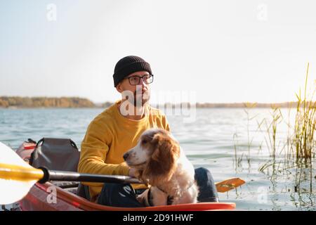 Homme avec un chien dans un canoë sur le lac. Jeune homme avec un épagneul dans un bateau de kayak, temps libre actif avec des animaux, compagnie, chiens d'aventure Banque D'Images