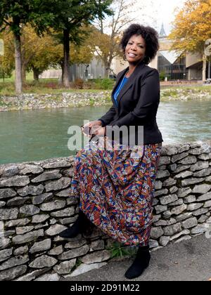 Portrait vertical d'une femme afro-américaine souriante et attrayante une veste noire et assise près d'une rivière Banque D'Images