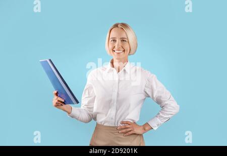 Portrait d'une femme entrepreneure positive dans un dossier de tenue de bureau avec des documents sur fond bleu studio Banque D'Images