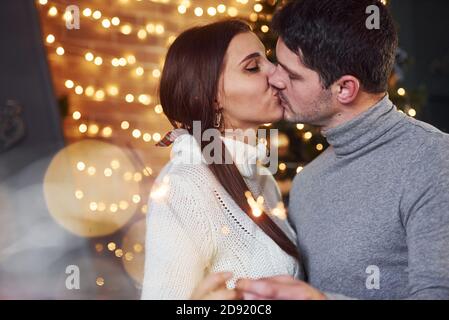 Couple embrassant à l'intérieur dans la chambre décorée de noël avec des étincelles dedans mains Banque D'Images