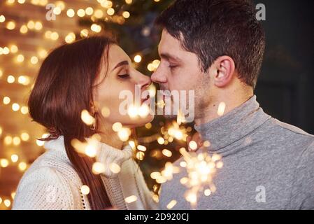 Couple embrassant à l'intérieur dans la chambre décorée de noël avec des étincelles dedans mains Banque D'Images