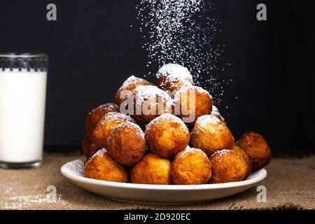 Les beignets frits sont saupoudrés de sucre en poudre. Il y a un verre de lait en arrière-plan Banque D'Images