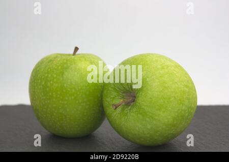 Une paire de pommes vertes de type doré sur un surface noire et arrière-plan blanc avec espace de copie Banque D'Images
