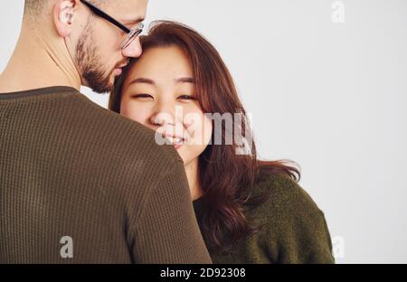 Un couple multiethnique heureux dans des vêtements décontractés est ensemble à l'intérieur dans le studio. Un homme de race blanche avec une petite amie asiatique Banque D'Images