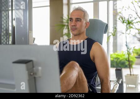 Homme persan mûr faisant pression sur les jambes à la salle de gym Banque D'Images