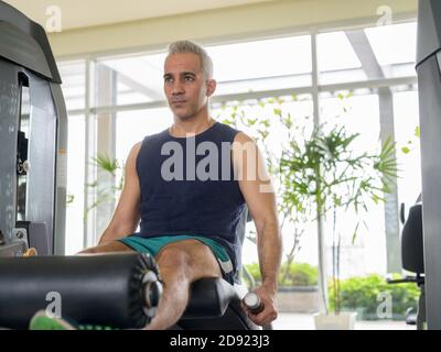 Homme persan mûr faisant un exercice d'extension de jambe au salle de sport Banque D'Images