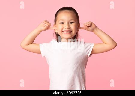 Enfant asiatique collant les doigts dans les oreilles et grimaçant Banque D'Images