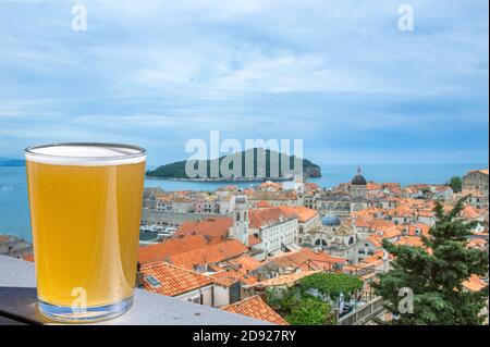 Verre de bière légère contre vue sur les toits rouges et la mer bleue depuis le mur de la ville de Dubrovnik, Dubrovnik, Croatie. Vue depuis le dessus du centre-ville. Banque D'Images