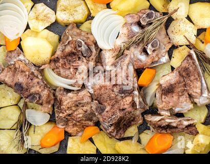 Compotée d'os de porc avec des pommes de terre, des oignons, des carottes, du romarin. Concept de fond alimentaire. Banque D'Images