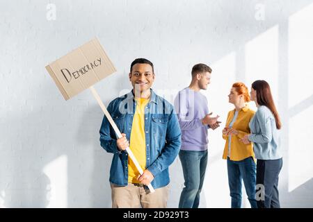 un indien heureux portant un écriteau de la démocratie tout en étant multiculturel des personnes partageant les mêmes vues qui parlent sur un arrière-plan flou Banque D'Images