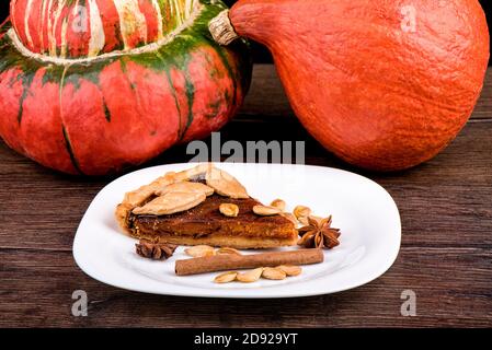 Tarte à la citrouille décorée de biscuits en forme de feuilles dans une assiette de cannelle, d'anis étoilé et de graines de citrouille. Assiette avec un morceau de tarte à la citrouille. Banque D'Images
