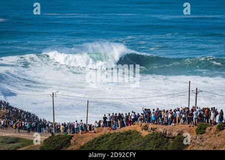 Les gens qui regardent le surfeur de grandes vagues monter sur une vague géante à la plage de Praia do Norte à Nazaré, au Portugal. Banque D'Images