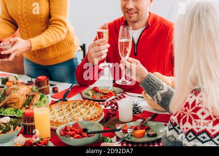 Vue courte d'une femme et d'un homme tenant des verres avec champagne, assis près de la famille à table Banque D'Images