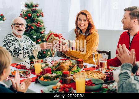 Femme et homme âgé tenant une boîte cadeau tout en étant assis avec famille à table de fête Banque D'Images