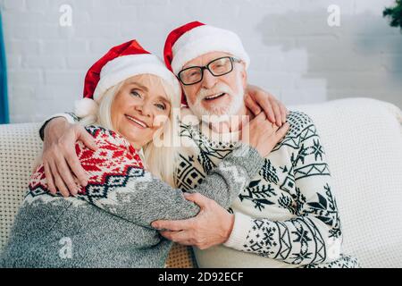 joyeux couple senior en chapeau de père noël embrassant tout en regardant appareil photo Banque D'Images