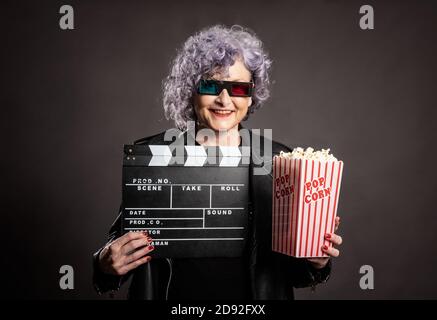 portrait d'une belle femme plus âgée tenant du pop-corn et du film clapper sur fond gris Banque D'Images