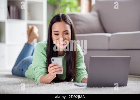 Gros plan photo de l'utilisation positive de l'ordinateur portable de travail de fille chinoise le téléphone intelligent vérifie la notification des réseaux sociaux et se trouve dans la moquette de l'hôtel intérieur Banque D'Images