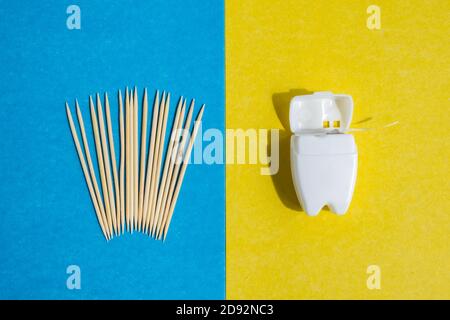 cure-dents sur fond bleu et fil dentaire dans un récipient blanc sur fond jaune, vue du dessus Banque D'Images