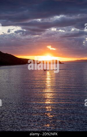 Kea, île de Tzia, destination Grèce. Coucher de soleil, lever de soleil orange à travers les nuages au-dessus de la mer Méditerranée. Le soleil se réfléchit sur l'eau. Photo verticale. Banque D'Images