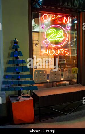 Ouvert 24 heures sur 24, panneau néon sur le café, arbre de Noël en bois avec guirlandes la nuit en hiver Banque D'Images