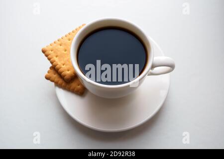 Tasse de café noir avec craquelins sur soucoupe sur blanc arrière-plan Banque D'Images