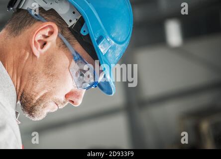 Travailleur de la construction dans ses 40 en Blue casque et yeux lunettes de sécurité profil Portrait. Jour ouvrable. Banque D'Images