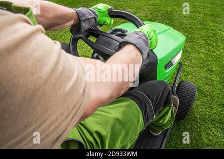 Caucasien Gardener sur son tracteur professionnel de fauchage d'herbe coupant l'herbe d'arrière-cour. Thème de l'industrie du jardinage et de l'aménagement paysager. Banque D'Images