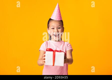 Bonne fille asiatique vous donnant boîte cadeau au studio jaune Banque D'Images