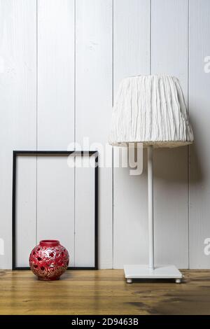 un cadre noir vierge, un porte-bougie rouge et une lampe sur la table avec un fond en bois blanc Banque D'Images