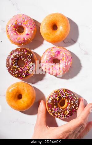 Beignets aux différentes glaçages, pâtisseries sucrées traditionnelles recouvertes de saupoudres sur fond de marbre blanc Banque D'Images