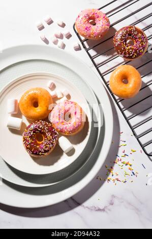 Beignets aux différentes glaçages, pâtisseries sucrées traditionnelles recouvertes de saupoudres sur fond de marbre blanc Banque D'Images