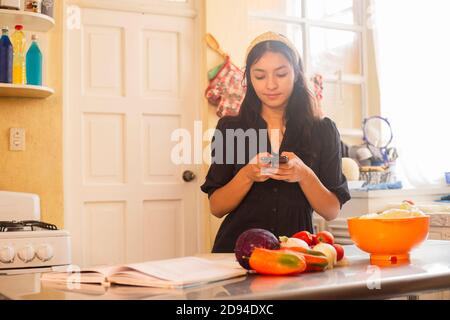 femme prenant photo de la nourriture pendant la cuisine - jeune femme préparer une délicieuse salade à la maison tout en utilisant son téléphone - Femme hispanique cuisant des aliments végétaliens Banque D'Images