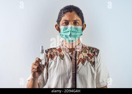 L'homme asiatique porte un masque chirurgical et tient un désinfectant pour les mains ou une bouteille anti-bactérienne. Virus pandémique concept Banque D'Images