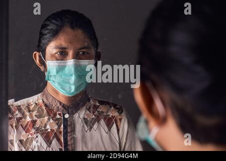 Potrait de l'homme asiatique avec masque médical et regardant dans le miroir. Prévention du concept de virus Banque D'Images