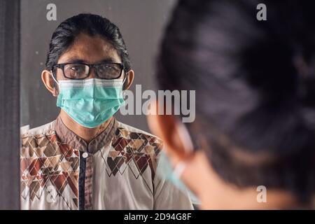 Potrait de l'homme asiatique avec masque médical et regardant dans le miroir. Prévention du concept de virus Banque D'Images