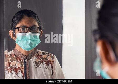 Potrait de l'homme asiatique avec masque médical et regardant dans le miroir. Prévention du concept de virus Banque D'Images