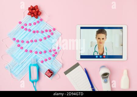 Joyeux Noël. plat avec thermomètre numérique, carnet, médecin sur appel vidéo sur tablette, arbre de noël fait à partir de masques médicaux, pilules an Banque D'Images