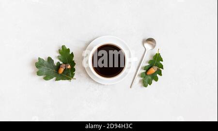 Tombez encore la vie avec une tasse de café noir, des feuilles de chêne et des glands. Café Acorn sur fond blanc. Vue de dessus. Pose à plat. Banque D'Images